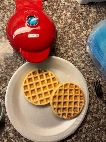 reviewer's red waffle maker next to plate of waffles