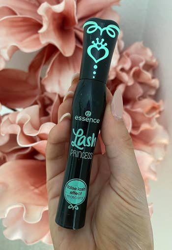 Hand holding Essence Lash Princess mascara conduit  successful  beforehand   of pinkish  angiosperm  backdrop