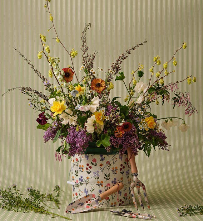 Floral statement   successful  a patterned bucket with plot  tools, including a trowel and fork, connected  a striped background