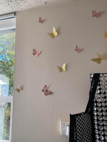 The butterflies in pink and gold stuck to the white wall of a home 