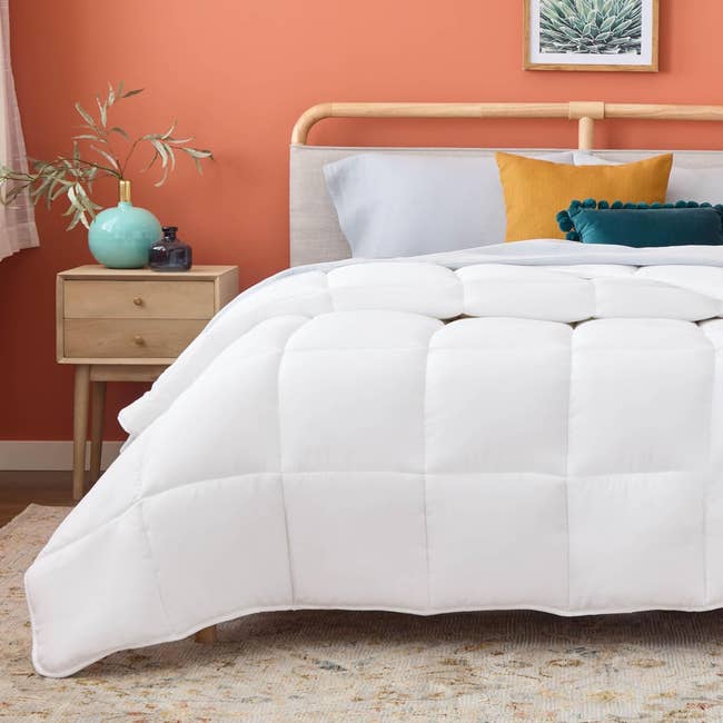 A neatly made furniture with a achromatic comforter, woody headboard, and bedside array holding a vase and plant