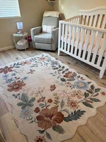Nursery with a floral rug, white crib, cushioned chair, and side table with a lamp, creating a cozy, inviting atmosphere