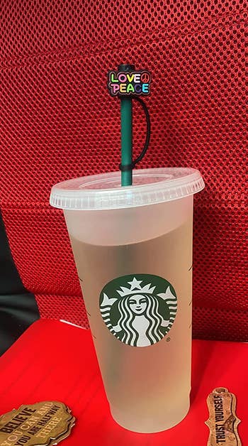 the straw cap cover that says Love and Peace attached to a starbucks cup, covering the straw
