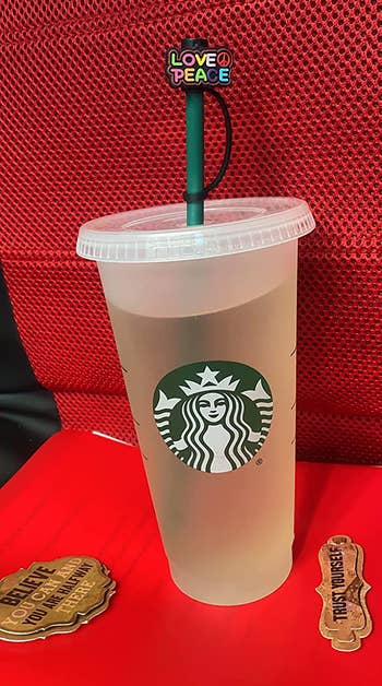 the straw cap cover that says Love and Peace attached to a starbucks cup, covering the straw