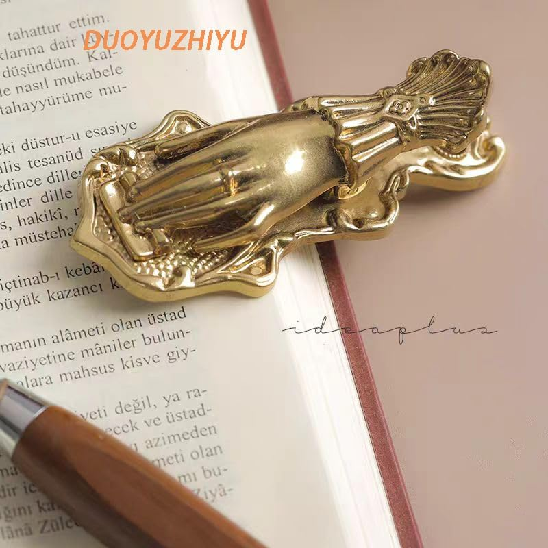 A gold hand-shaped bookmark rests on an open book near a pen, with partial visible text around it