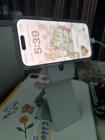 A smartphone on a stand displays a cute animal-themed wallpaper with a digital clock reading 5:39