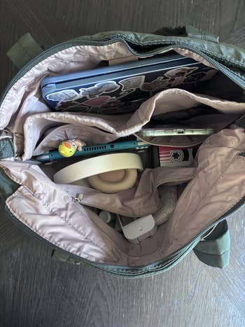 Open backpack with laptop, headphones, pink cardholder, tablet stylus, and a small figurine. Items suggest convenience for tech and travel
