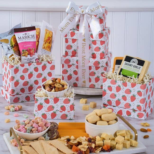 Gift set with strawberry-themed boxes containing various snacks, candies, and cheese, topped with a ribbon reading 