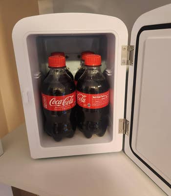 Mini fridge open, showing 4  Coca-Cola bottles inside