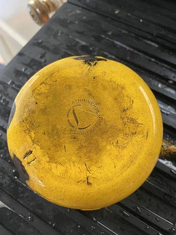 Worn yellow pan with visible scratches and brand engraving on the bottom, placed on a dark surface