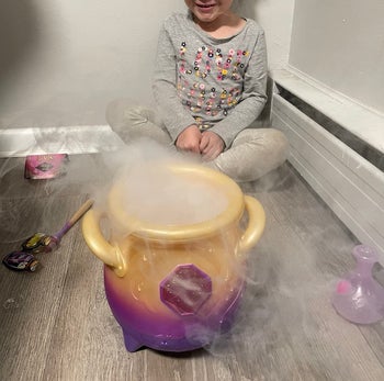 A child sitting near a toy cauldron with smoke coming out of it