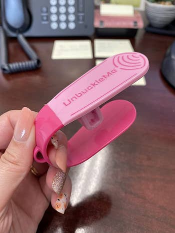 reviewer holding the pink seat buckle release tool