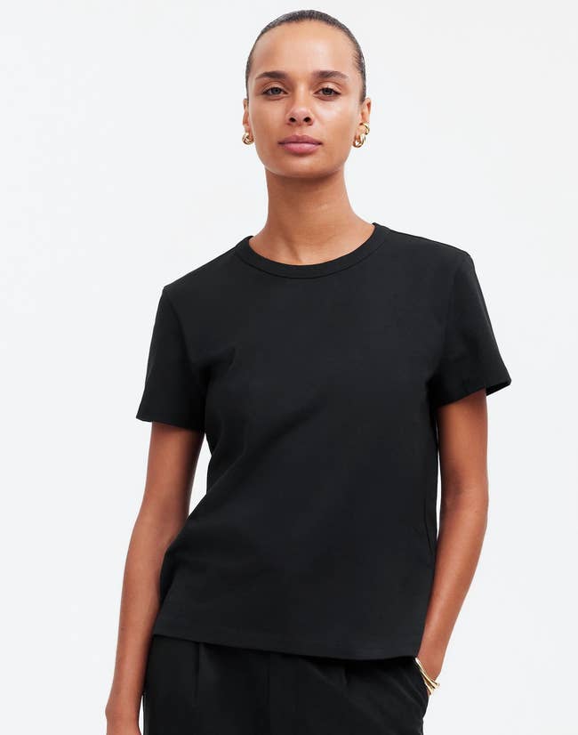 Person wearing a simple, tailored black t-shirt, styled with gold hoop earrings