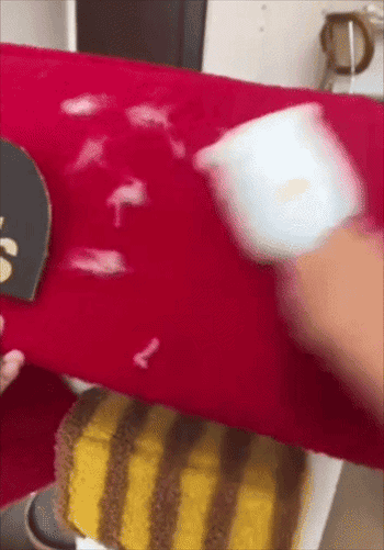 A manus uses a cloth shaver to region lint from a fuzzy reddish surface, demonstrating a cleaning product's effectiveness