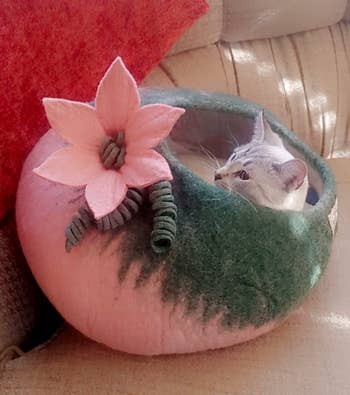 reviewer's cat laying in the wool cave bed with a pink flower on it