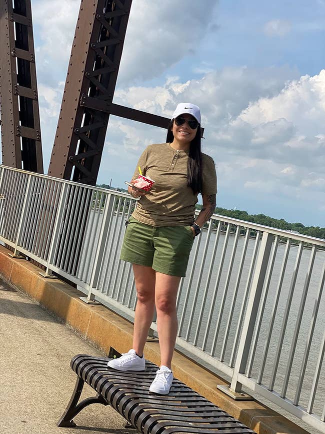 Person lasting  connected  a span  successful  casual attire, holding a cupful  with a smile, wearing shorts and a cap, suitable for a relaxed outdoor day
