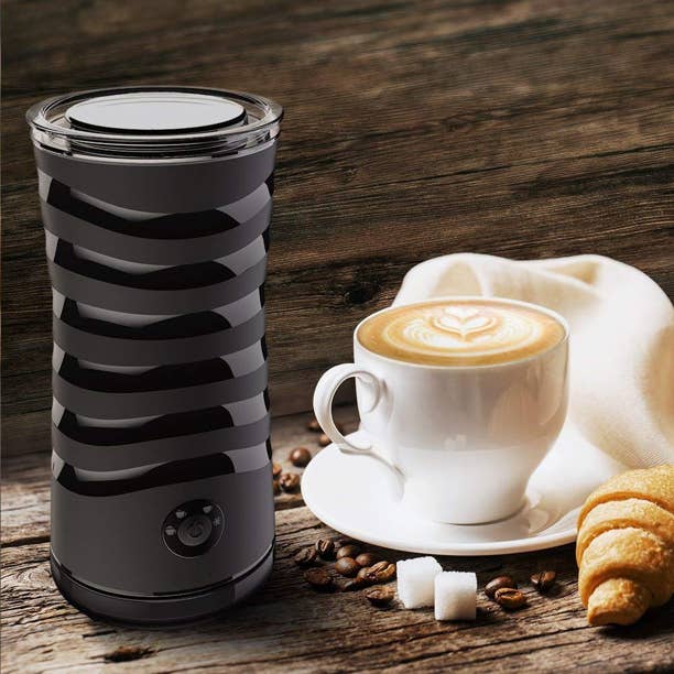 Black milk frother and steamer with ridges along the center next to cup of coffee on a white plate