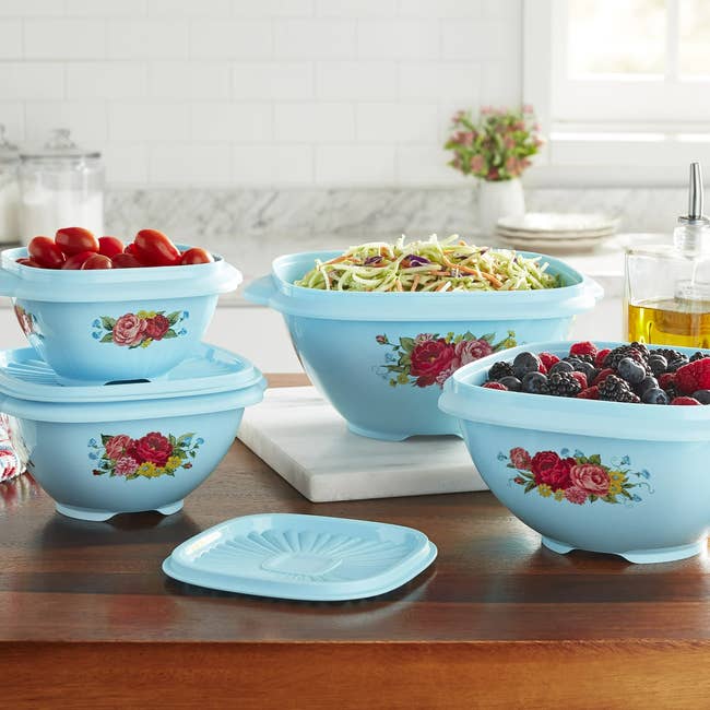 Four decorative room  bowls with floral patterns clasp  assorted  nutrient  items similar  tomatoes, salad, and berries, displayed connected  a room  counter