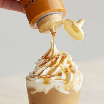 Hand drizzles caramel syrup onto whipped pick  topping connected  a beverage
