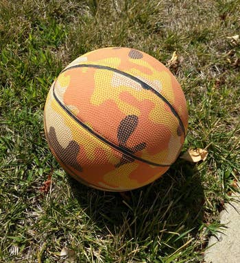 a reviewer photo of a basketball with an orange camo print sitting in the grass 