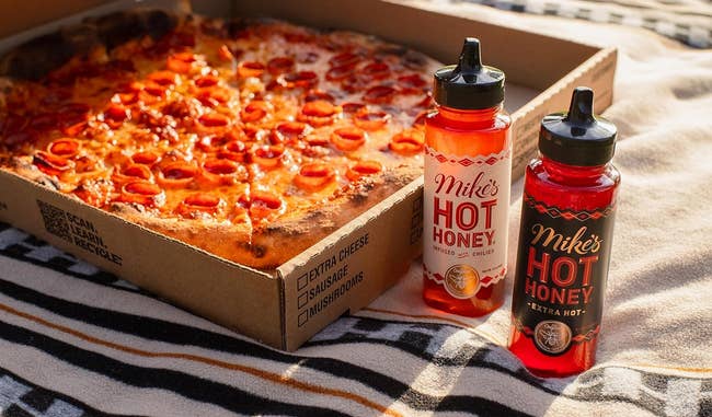two bottles of hot honey next to a box of pepperoni pizza