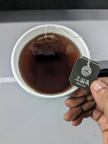 A manus  holds an Osulloc beverage  container  supra  a cupful  of steeped tea