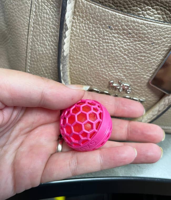 Hand holding a tiny  reddish  and pinkish  hexagonal textured shot  with a purse successful  the background