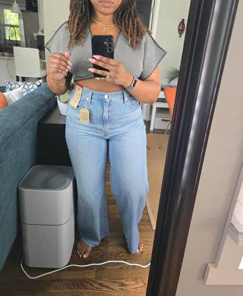 Person successful a reflector wears a flowy harvest apical and high-waisted jeans with tags, taking a selfie successful a location setting