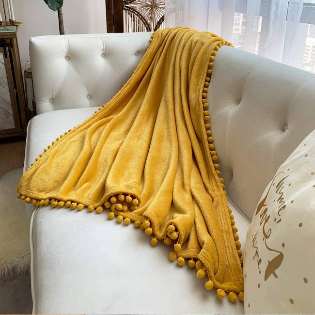 Mustard Yellow throw blanket with pom poms on edges draped over couch