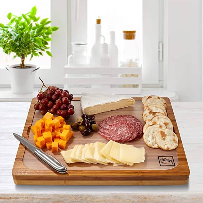 a bamboo cutting board with meats, cheeses, fruits, and crackers