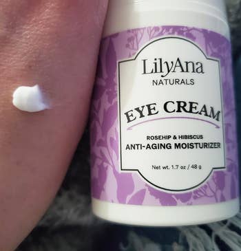 A person's hand next to a bottle of LilyAna Naturals Eye Cream with a dab of product on top