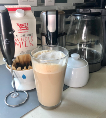 reviewer photo of the frother next to a glass filled with a latte