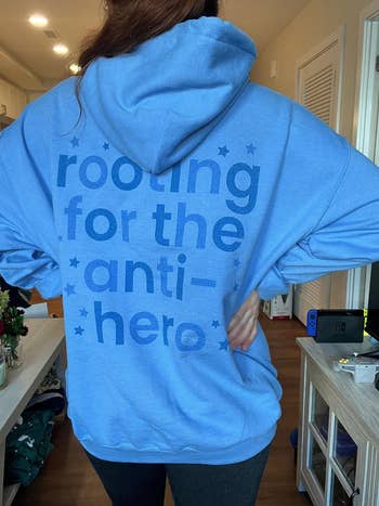 a model showing the back of a blue hoodie that says rooting for the anti-hero