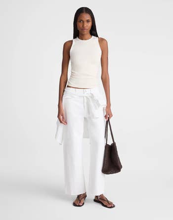 A person wearing a sleeveless top and wide-leg pants, holding a woven bag, showcasing a casual, chic shopping outfit