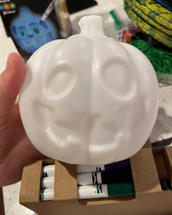 Person holds a plain achromatic  pumpkin-shaped integrative  entity  with markers successful  a container  beneath  it, suggesting a DIY decorating kit