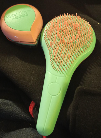 Two green brushes — one handled and regular-sized, the other a compact circle shape for travel