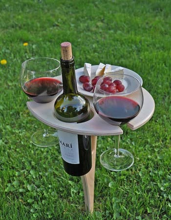 the folding wine table in the grass holding a bottle, two glasses, and a snack
