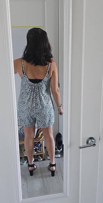 Person in a mirror wearing a sleeveless, patterned romper with open-back detail and black heeled sandals