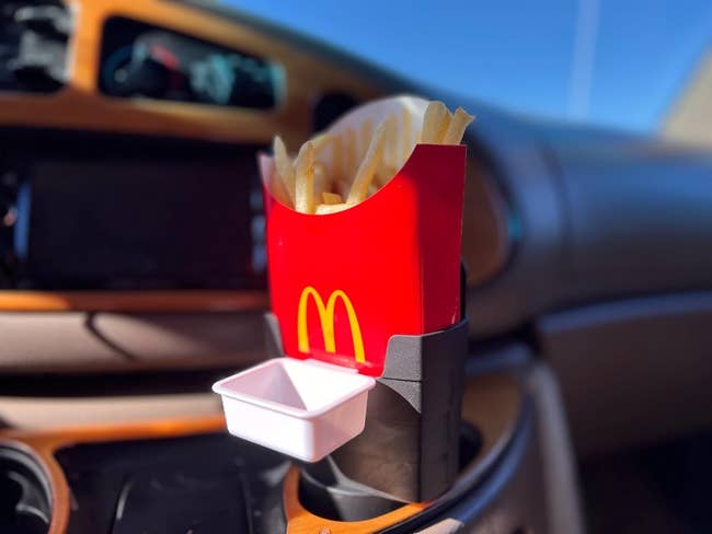 A small black container propped in a drink holder holding up reviewers carton of fries in car's cup holder