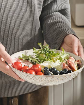Person holding a decorative vessel filled with cherry tomatoes, blueberries, arugula, figs, and different caller produce