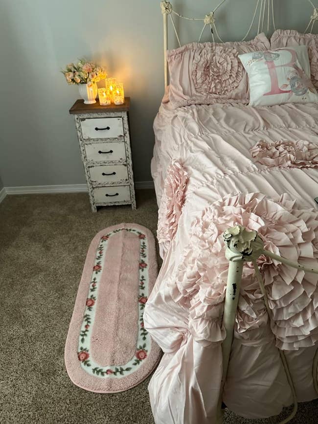 Bedroom with ruffled bedding and matching floral rug, vintage-style side table with candles. Perfect for a feminine decor theme