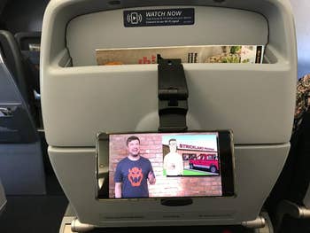reviewer photo of phone playing video, clamped onto back of airplane seat