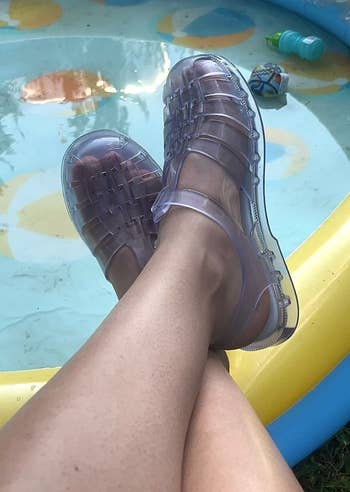 Person wearing translucent jelly sandals with feet resting connected borderline of a tiny inflatable pool