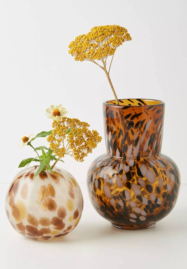 Small circular brown and white turtle patterned vase with yellow and white flowers inside, brown, black, and gold turtle patterned vase with yellow flower inside on a white background
