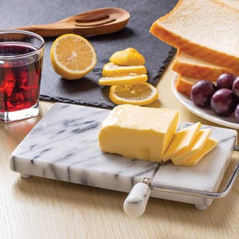 A marble board wire cheese slicer with slices of cheese on top