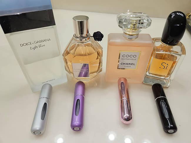 reviewer image of the four mini atomizers next to large perfume bottles