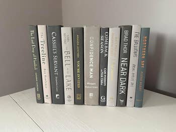 A row of eleven hardcover books standing on a shelf, showcasing various titles and authors