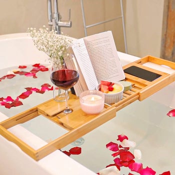 photo of a book, a glass of wine, a dessert, and a candle on the tray over a bath tub