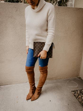 reviewer wearing brown boots with blue jeans and cream turtle neck