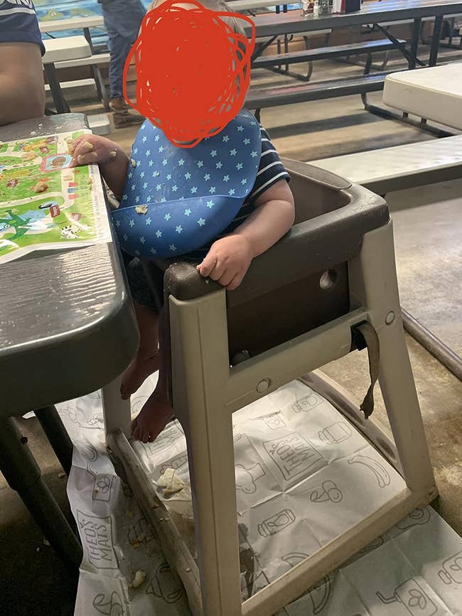 Child in highchair with star-patterned outfit at table, interacting with a placemat
